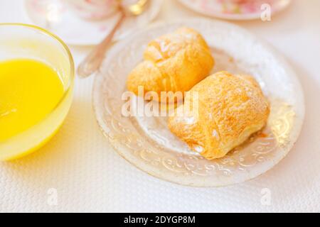 Two crispy croissants on a silver vintage plate and honey in glass on the white sunny table. Stock Photo