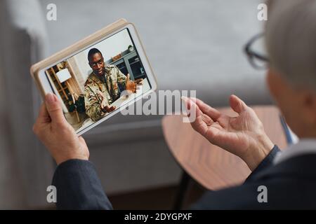 Rear view of woman using digital tablet for online conversation with African soldier Stock Photo