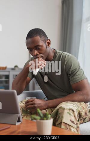 Sad African soldier sitting on sofa looking at digital tablet he getting a sad email Stock Photo