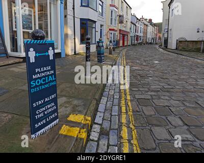 Covid-19 social distancing reminder signs on street bollards in the rural North Yorkshire town of Staithes Stock Photo