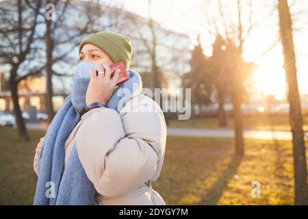 Young woman in protective mask talking on the phone while walking in the city Stock Photo