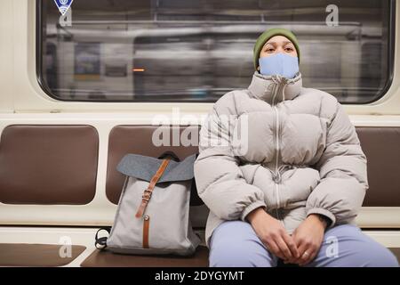 Young woman in mask and in warm clothing sitting on a train underground Stock Photo