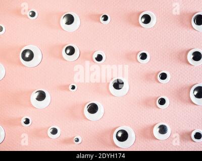 many flat plastic doll eyes on pink paper background Stock Photo