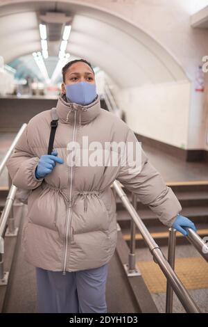 Young woman in protective mask and gloves standing on escalator in the underground Stock Photo