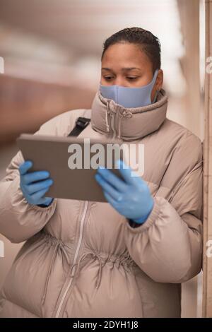 Young woman in mask and in protective gloves using digital tablet while waiting for the train Stock Photo