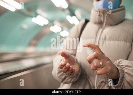 Close-up of woman applying antiseptic on her hands and protecting herself during pandemic while standing on escalator Stock Photo