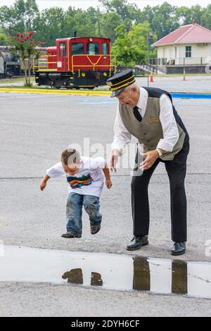 Alabama Calera Heart of Dixie Railroad Museum,senior man male conductor's uniform boy kid child,jumps jumping puddle, Stock Photo