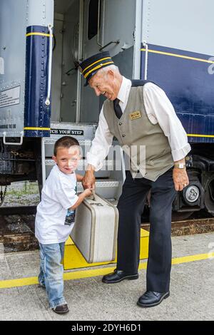 Alabama Calera Heart of Dixie Railroad Museum,boy kid child visitor senior man male conductor's uniform volunteer,helping taking lifting luggage suitc Stock Photo