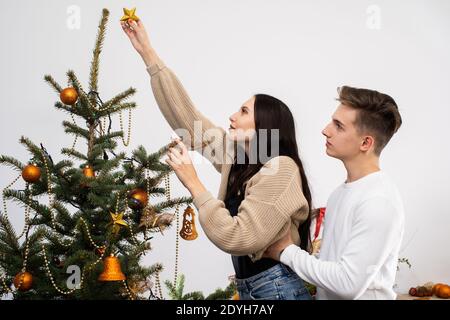 A golden meringue star is put on the top of the Christmas tree by a couple in love decorating the entire Christmas tree for Christmas. Stock Photo