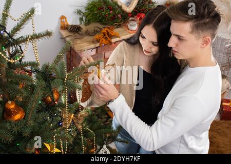 A golden meringue star is put on the top of the Christmas tree by a couple in love decorating the entire Christmas tree for Christmas. Stock Photo