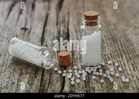 Granules of homeopathic medicine in small glass flasks and scattered on an old wooden table. Stock Photo
