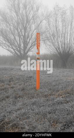 Orange coloured metal pole with graffitis standing lonely in the fields on a foggy grey day Stock Photo