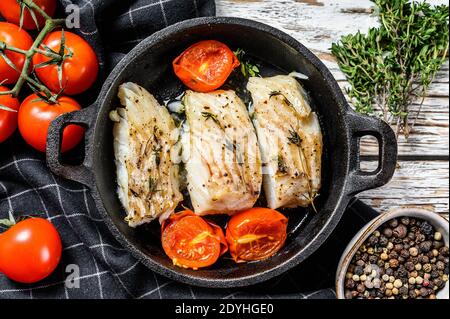 Fried cod fish fillet with spice in a cast iron pan. White background. Top view. Stock Photo