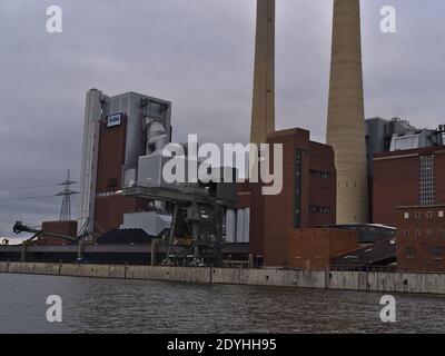 View of coal-fired Heilbronn Power Station operated by Energie Baden-Württemberg (ENBW) with heap of coal and port crane on th shore of Neckar river. Stock Photo