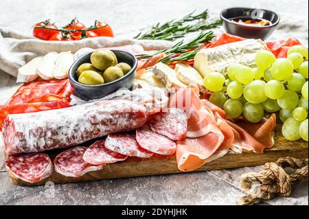 Italian antipasto, wooden cutting board with prosciutto, ham, parma, goat and Camembert cheese, olives, grapes. antipasti. Gray background. Top view Stock Photo