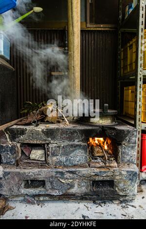Rakan, a kaiseki restaurant run by chef Atsuko Kato, on the Izu Peninsula, Japan. Rice simmers over a wood fire in the traditional stone stove as a hand holds a ladle ready. Stock Photo