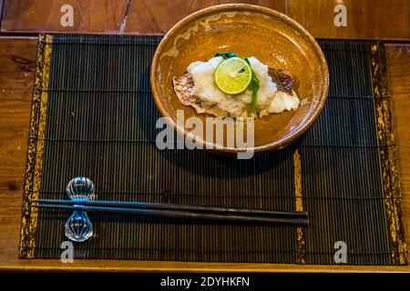 Rakan, a kaiseki restaurant run by chef Atsuko Kato, on the Izu Peninsula, Japan. Grilled fish with grated daikon radish and a lime rests in a ceramic bowl. Stock Photo