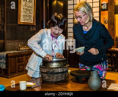 Rakan, a kaiseki restaurant run by chef Atsuko Kato, on the Izu Peninsula, Japan. Rice from the traditional cooker is served at the table as a guest smiles in the background. Stock Photo
