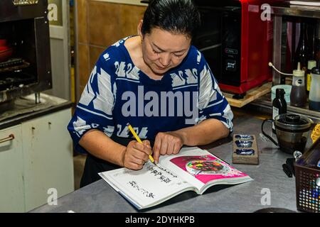 Rakan, a kaiseki restaurant run by chef Atsuko Kato, on the Izu Peninsula, Japan. Atsuko Kato completes the calligraphic dedication in her book. Stock Photo