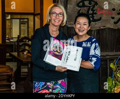 Rakan, a kaiseki restaurant run by renowned chef Atsuko Kato, on the Izu Peninsula, Japan. She presents the calligraphic dedication in her book with travel journalist Angela Berg in front of the restaurant. Stock Photo