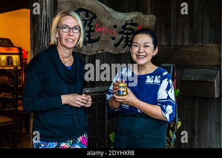 Rakan, a kaiseki restaurant run by chef Atsuko Kato, on the Izu Peninsula, Japan. The chef and travel journalist Angela Berg are laughing in front of the restaurant entrance; Atsuko Kato is holding a jar of German honey. Stock Photo