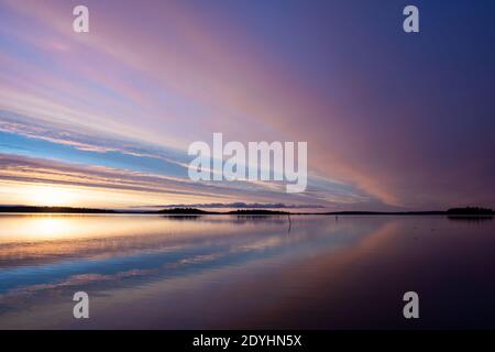 Beautiful landscape with sunrise over the lake this winter morning. Clouds and sky color reflections in the calm water. Photo taken in Sweden. Stock Photo