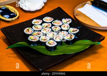 Freshly sliced futomaki sushi pieces filled with egg, cucumber, fish flakes and surimi are arranged in a star pattern on a black plate with a leaf garnish – Kayoko Kawamura's bento workshop, Izunokuni, Izu Peninsula, Japan. Stock Photo