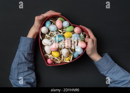 Children holding a Heart shaped box with colorful Easter eggs. Black background. Gift for Easter. Stock Photo