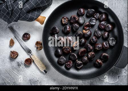 Fried chestnuts in a pan on a wooden table. White background. Top view Stock Photo