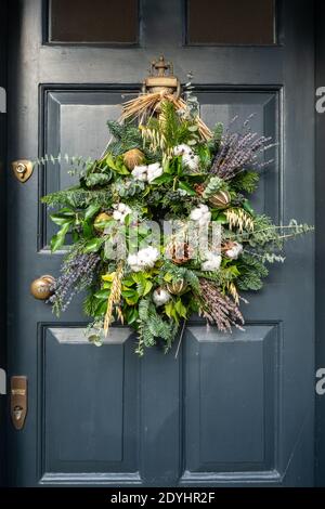 Christmas wreath made with ivy leaves, berries, cones and lavender on a black door, UK. Natural seasonal decorations. Stock Photo