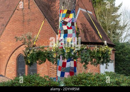 Natural christmas decorations made with holly and pine around a tree with a blanket made of crocheted squares outside St Mary's Church, Ash Vale, UK Stock Photo