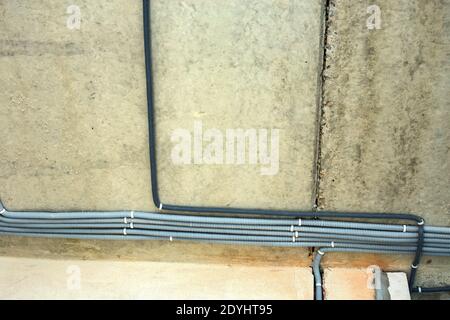 Electrical cables laid in protective corrugation installed on the ceiling and wall in a room under construction works. Stock Photo