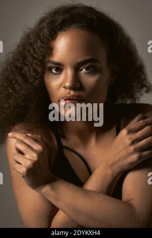 Feeling afraid, showing fear or anxiety African American young woman standing covered with hands crossed on her chest isolated on grey background Stock Photo