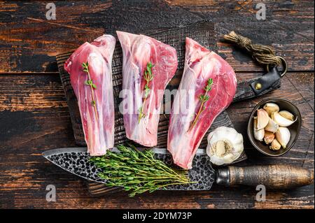 Raw lamb shanks meat on a cutting board with herbs. Dark wooden background. Top view Stock Photo