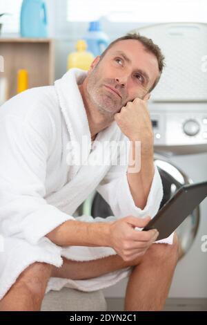 pensive man wearing bathrobe doing laundry Stock Photo