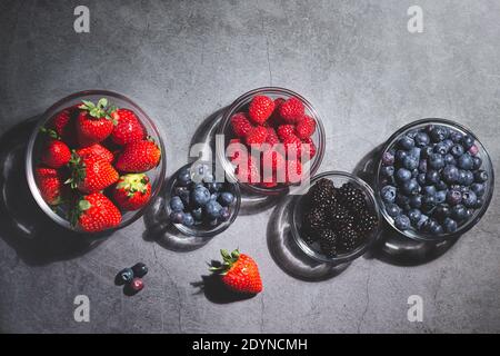 Assorted berries in glass bowls on dark background top view. Stock Photo