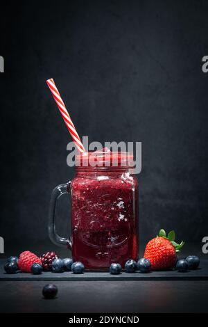Berries Smoothie in Glass Jar with Straw and assorted  berries on dark background. Stock Photo