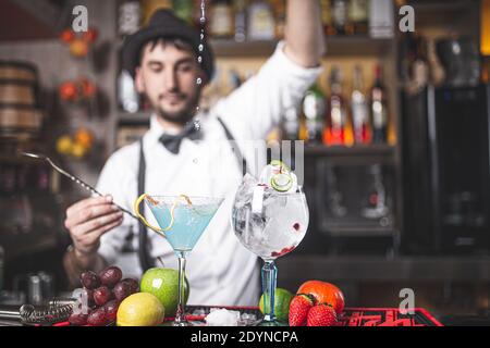 Expert barman making cocktail at night club with hat and bow tie. Drops falling in the cup. Stock Photo