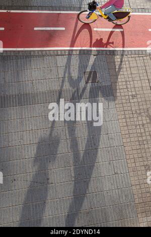 Cyclist riding on red urban bike lane in Las Palmas de Gran Canaria,bike shadow.  Urban bike lane concept. Stock Photo