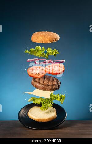 Flying burger on  wooden base and blue background. Stock Photo