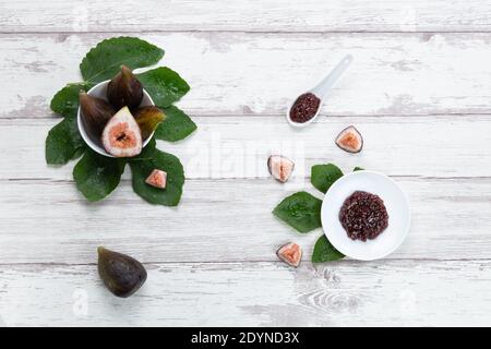 Fig jam with figs, fig leaves and white spoon with jam on White wood background. Stock Photo