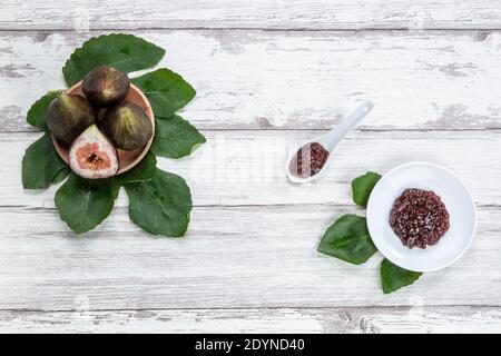 Fig jam with figs, fig leaves and white spoon with jam on White wood background. Stock Photo