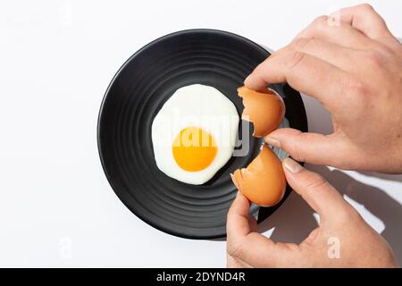 Hands cracking Fried egg on black plate on  white background. Cooking and food concept. Stock Photo