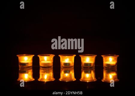 A row of burning candles reflecting on the desk with black background Stock Photo