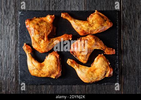 crispy roasted chicken legs served on a black slate tray on a dark wooden table, horizontal view from above Stock Photo