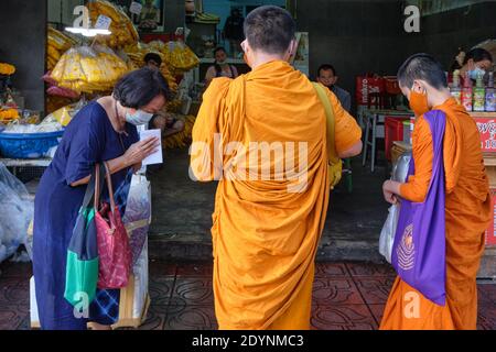A Thai woman bowing and asking for blessings fro two young Buddhist novice monks; during the monks' traditional daily alms round, in Bangkok, Thailand Stock Photo