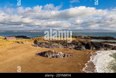 A view of Twr Bach and the Snowdonia mountains across Porth Twr Mawr on Llanddwyn island, Anglesey Stock Photo