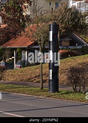 Modern black colored traffic enforcement camera for speed control at village entrance with road in front on sunny winter day. Stock Photo