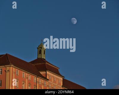 Historic building with pink colored decorated facade and small bell tower on the roof in beautiful evening light with moon visible in the blue sky. Stock Photo