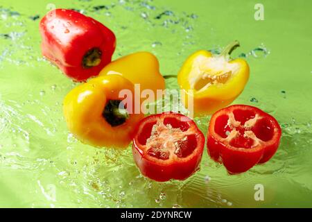 Red and yellow paprika in water splashes on a green background. Stock Photo